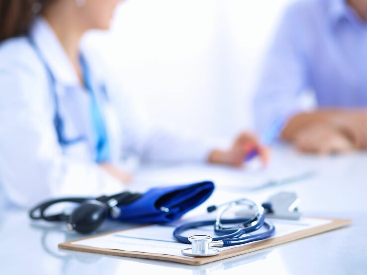Beratungsgespräch in Arztpraxis, weibliche Ärztin mit blauem Stethoskop spricht mit Patient.