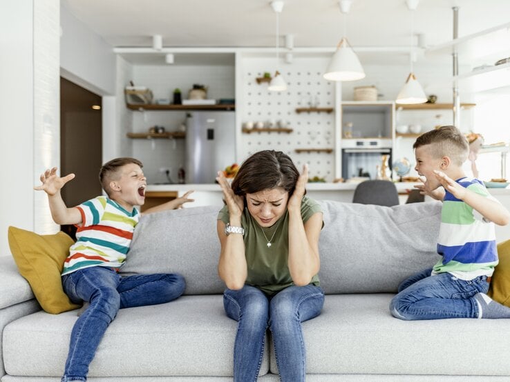 Kinder schreinen sich gegenseitig an. Mutter sitzt dazwischen und hält sich die Ohren zu. | © Getty Images/ljubaphoto