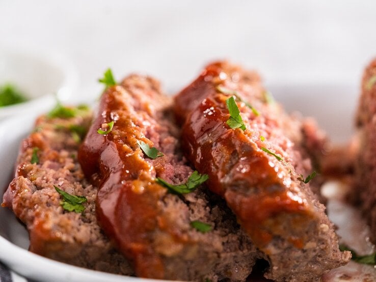 Hackbraten mit Schmorgemüse und Petersilie bestreut. Nah und in Scheiben geschnitten auf weißem Teller und mit weißem Hintergrund fotografiert