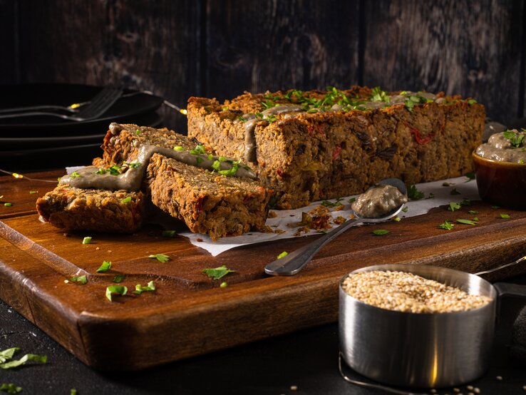 Auf einem großen Holzbrett liegt ein angeschnittener veganer Nussbraten mit etwas Soße beträufelt, drumherum eine Lichterkette und dunkler Hintergrund.