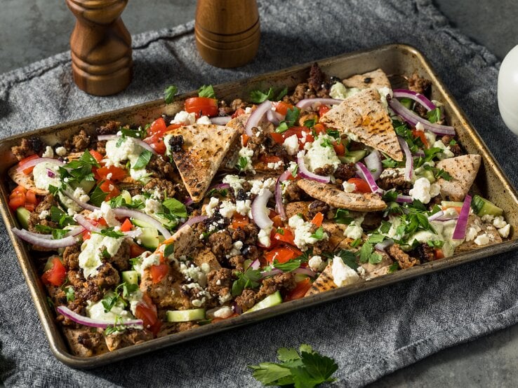 Gewürztes Hackfleisch mit Pita-Dreiecken und frischem Gemüse auf einem metallischen Backblech.