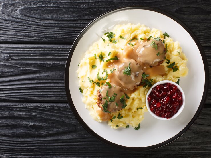 Von-Oben-Ansicht eines Tellers mit finnischen Hackbällchen, cremiger Soße und Kartoffelbrei. Daneben steht eine Schale Kompott. 