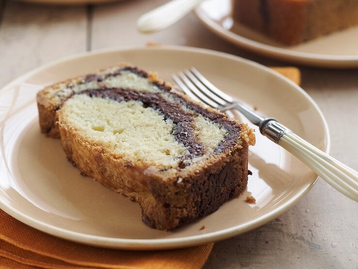 Ein heller Tisch mit mehreren weißen Tellern auf dem jeweils ein Stück Marmorkuchen mit Nutella liegt. Am Rand des Tellers eine Gabel mit weißem Griff und darunter eine gelbe Serviette.