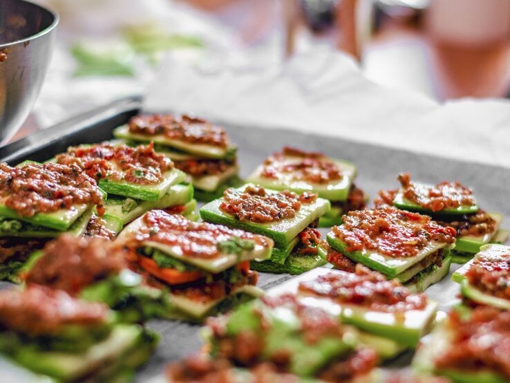 Vegane Zucchini-Lasagne-Schiffchen mit Tomatensoße portioniert auf einem Backblech.