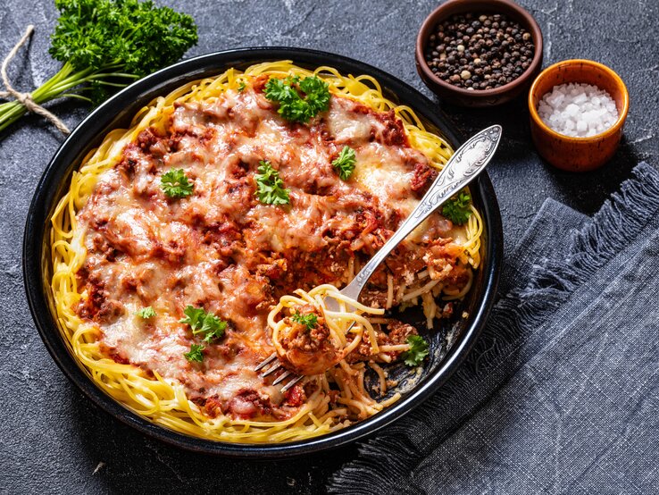 Spaghetti in fruchtiger Hackfleisch-Ricotta-Sauce auf schwarzem Teller. Alles auf dunklem Untergrund von schräg oben fotografiert.