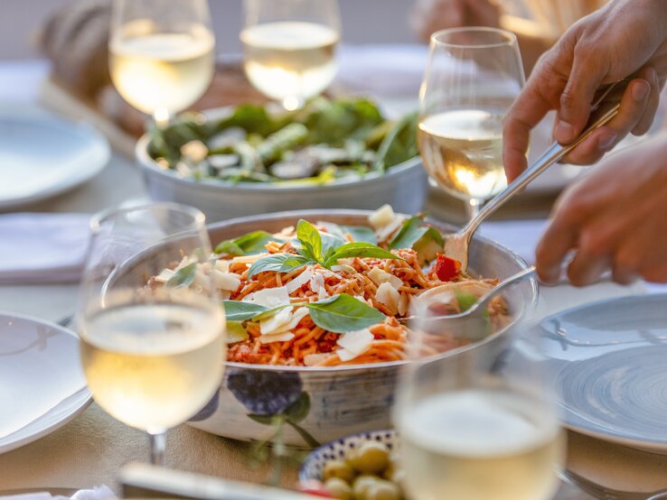 Silberfarbene Schüssel gefüllt mit Spaghett-Salat umrundet von Weingläsern.