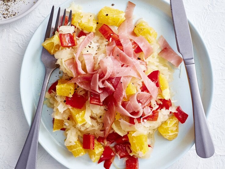 Sauerkrautsalat mit Orange und Schinken auf Teller angerichtet.