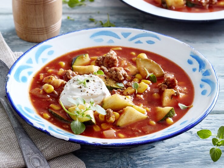 Auf einem tiefen Teller ist eine Portion Zucchini-Tomaten-Eintopf mit Hack serviert. Sie wird mit Frischkäse verfeinert.