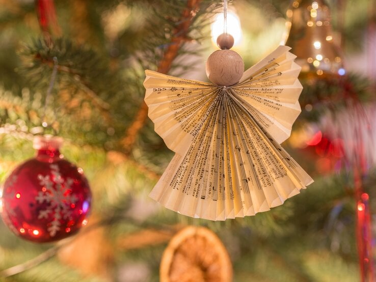 Selbst gebastelter Engel aus Notenblättern hängt am Weihnachtsbaum.