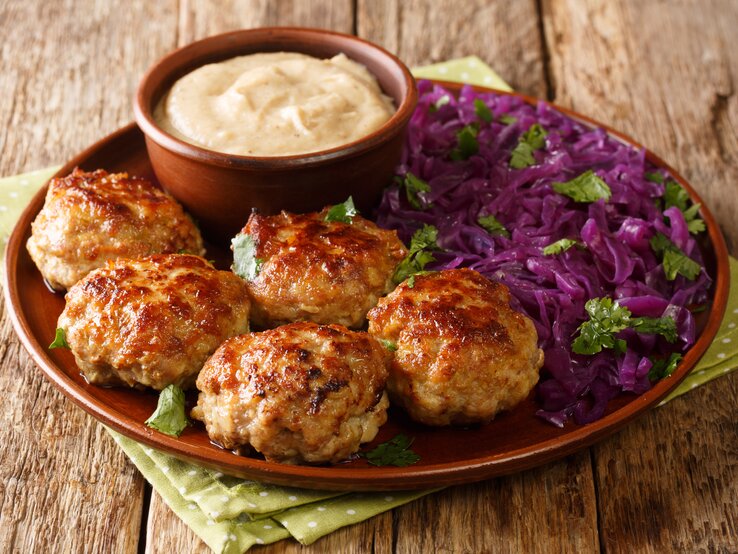 Brauner Teller mit Frikadellen, Dip und Rotkohl auf Holztisch. 