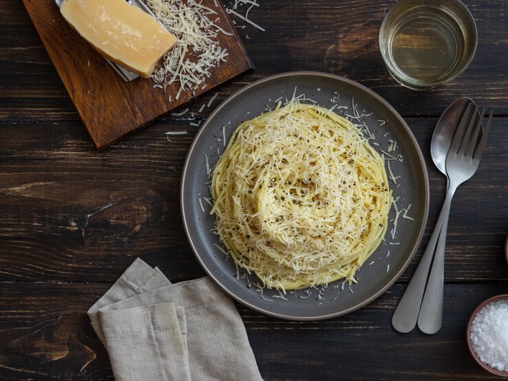 Spaghetti mit geriebenem Käse auf Holztisch.
