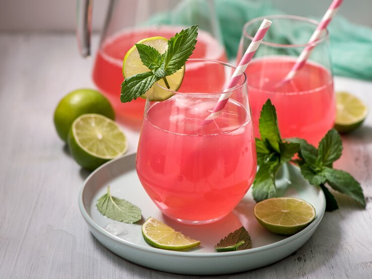 Zwei Gläser Rhabarber-Holunder-Spritz mit Strohhalmen, Minze und Limettenscheiben.