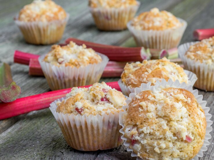 Mehrere Muffins auf einem Holztisch mit Rhabarberstangen.