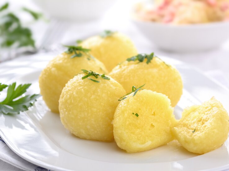 Auf einem weißen Teller liegen mehrere hausgemachte Kartoffelknödel, die mit Petersilie bestreut sind.