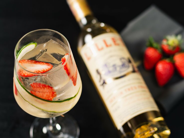 Lillet Gin Tonic in Weinglas mit Lillet-Flasche und Erdbeeren. Draufsicht.