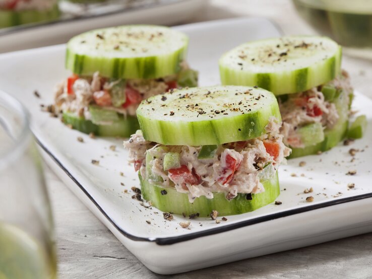 Auf einer weißen Porzellanschale sind drei kleine Gurken-Häppchen mit Thunfisch. Es handelt sich um Fingerfood.