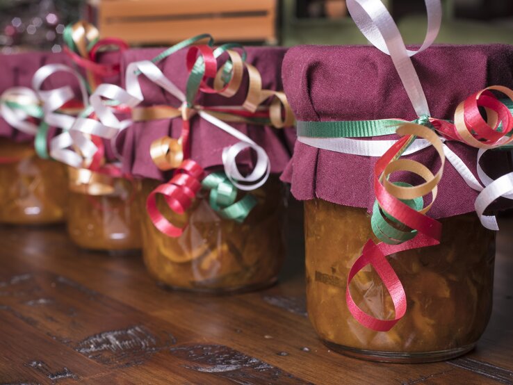 Selbst gemachte Marmeladen in Gläsern stehen mit Schleifen und lila Stoff auf dem Tisch.