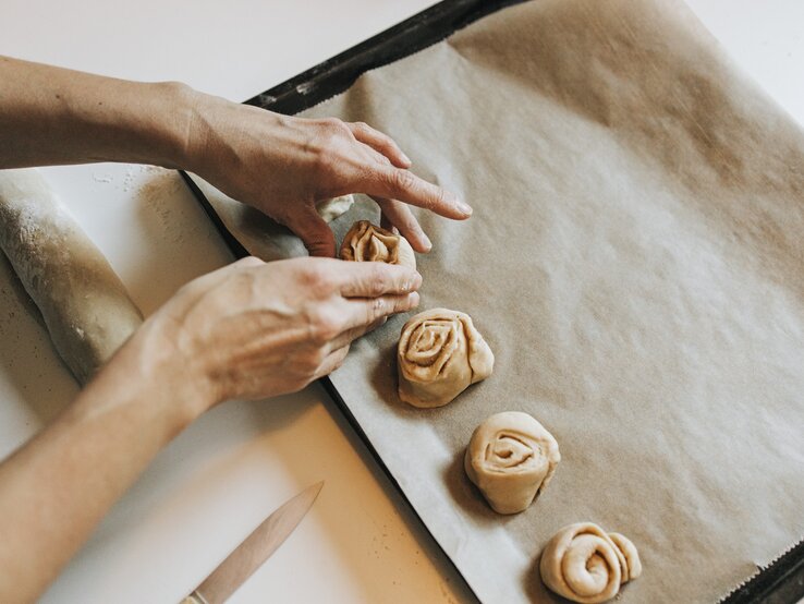 Person drapiert ungebackene Zimtschnecken auf einem Blech mit Backpapier.