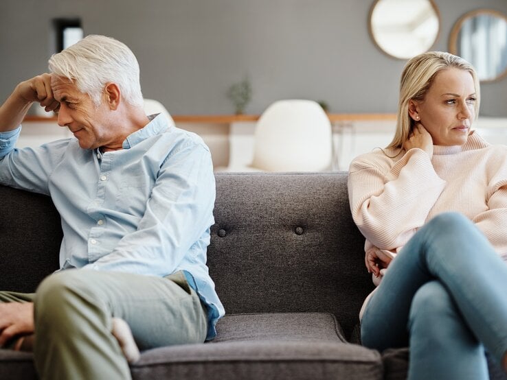 Älteres Paar, das auf einer Couch sitzt und sich offensichtlich in einem Konflikt befindet.