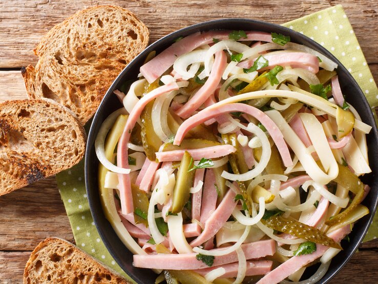 Vogelpersektive: In einer Schüssel ist ein Schweizer Wurstsalat . Daneben lieben drei Scheibe Brot.