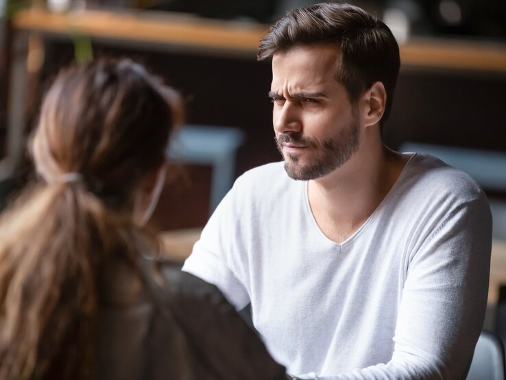 Mann und Frau sitzen sich in einem Café gegenüber. Der Mann hat einen besorgten oder verwirrten Gesichtsausdruck.