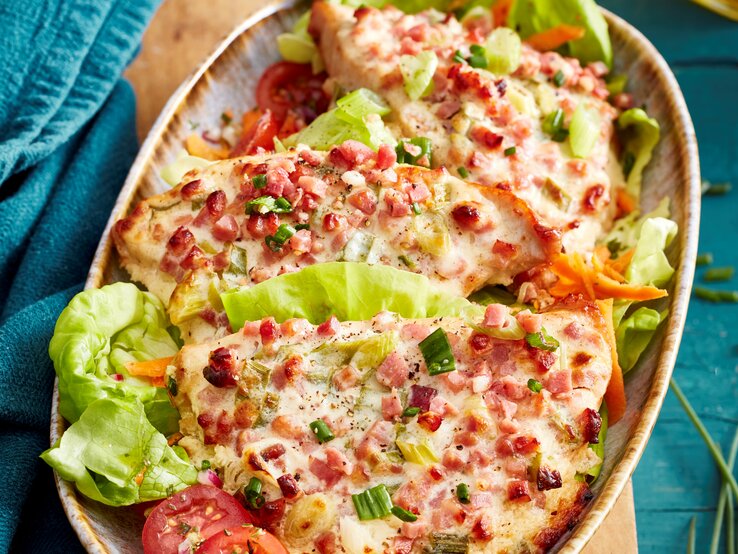 Flammkuchen-Schnitzel mit Salatblättern in einer Schale vor Hintergrund mit blauem Stoff. 