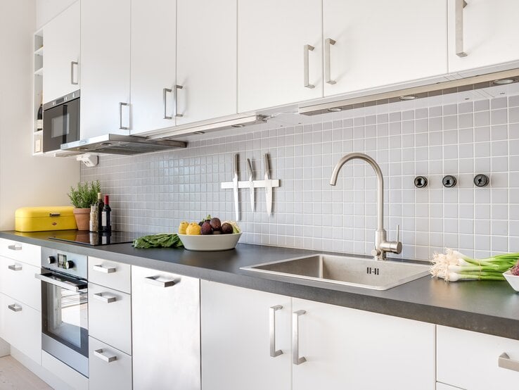 Moderne Küche mit einem eleganten und sauberen Design. Die Küchenzeile ist in Weiß gehalten, mit flächenbündigen Schränken und Edelstahlgriffen. 