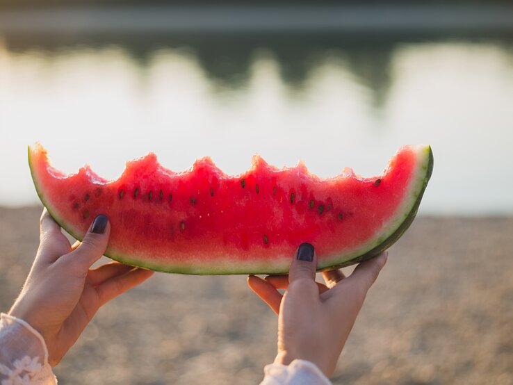 Eine Frau hält eine angebissene Scheibe Wassermelone in die Luft. 