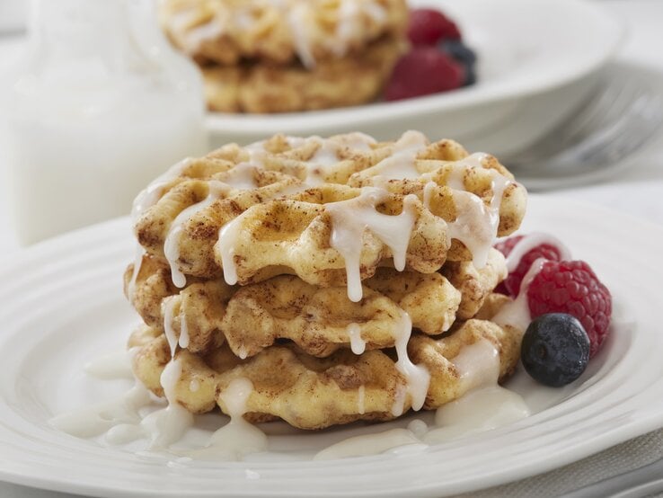 Drei Zimtschnecken-Waffeln mit Zuckerguss und Früchten auf weißem Teller. 