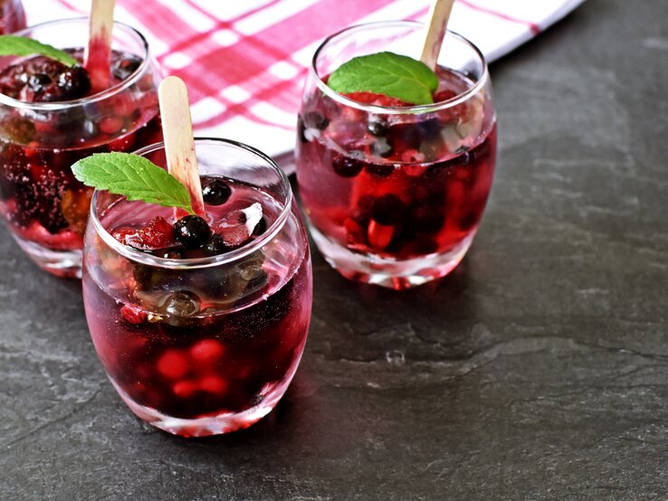 Drei Gläser mit Lillet Hot Berry auf einem grauen Steintisch.