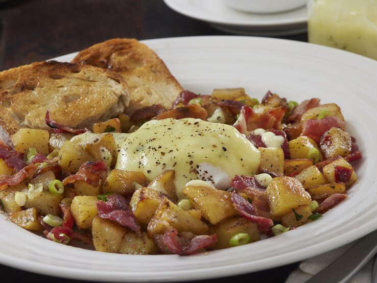 Bauernfrühstück mit Speck und Kartoffeln, pochiertem Ei und Sauce hollandaise auf einem weißen Teller. 