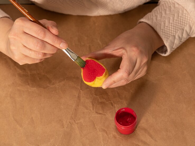 Eine Frau bemalt mit roter Farbe einen herzförmigen Kartoffelstempel.