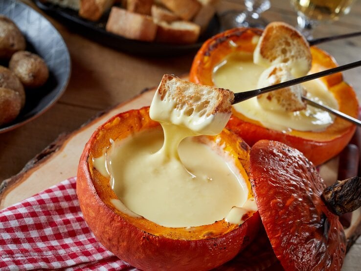 Käse-Fondue im Kürbis auf einem rustikalen Tisch mit rot-weiß-karierter Tischdecke.