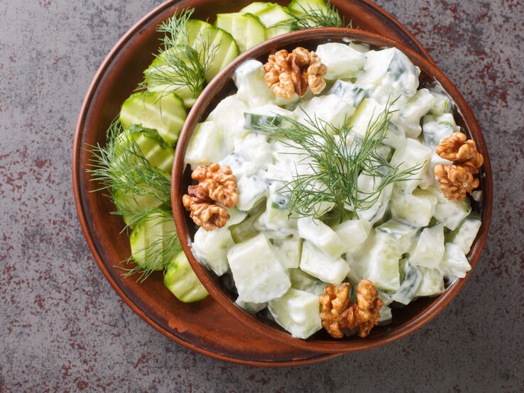 Bulgarischer Gurkensalat mit frischem Dill, Joghurt und ganzen Walnüssen, serviert in einer dunklen Keramikschale auf steinernem Untergrund. 