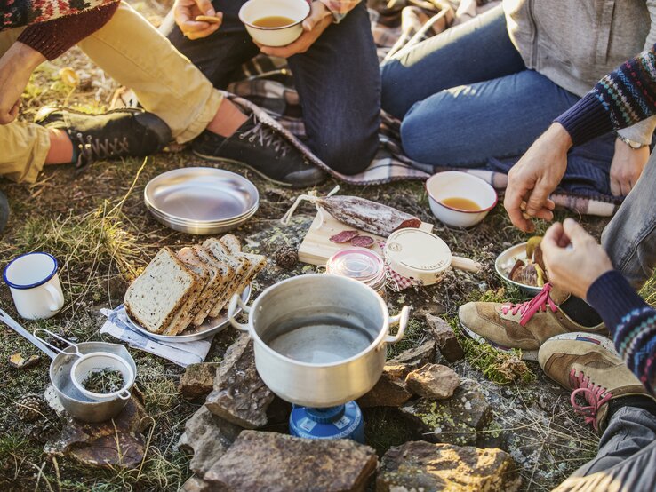 Eine Gruppe an Freunden frühstücken beim Camping-Ausflug.