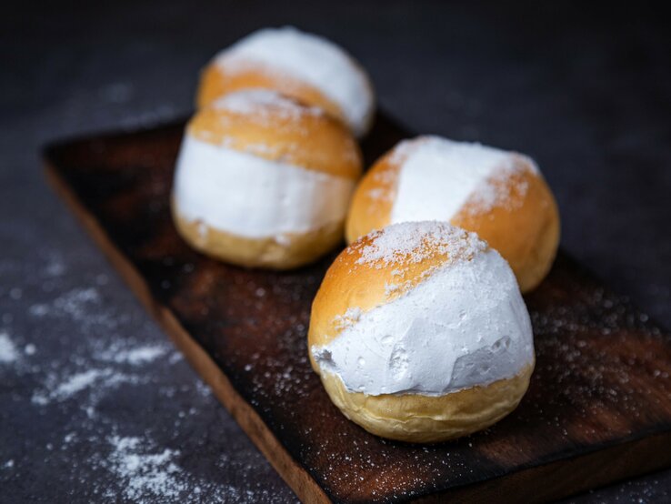 Vier der gefüllten Milchbrötchen auf einem dunklem Holzbrett mit schwarzem Unter- und Hintergrund.