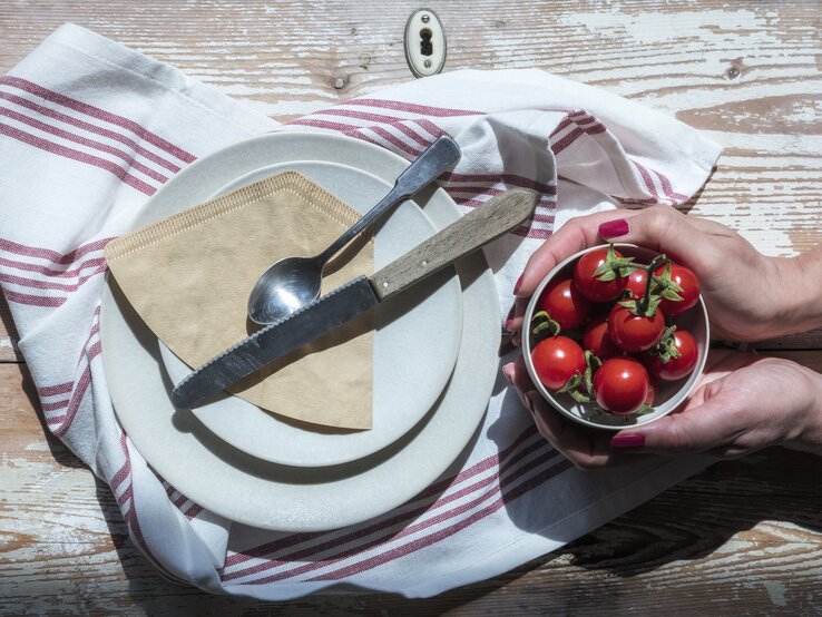 Kaffeefilter sollen zum Polieren von Besteck benutzt werden. Die Papiertüten liegen auf einemTeller. Man sieht Hände einer Frau, die eine Schüssel mit selbst angebauten Tomaten hält.