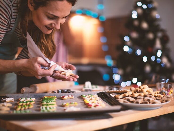 Frau verziert verschiedene ausgestochene Weihnachtsplätzchen, die auf einem Backblech liegen. 