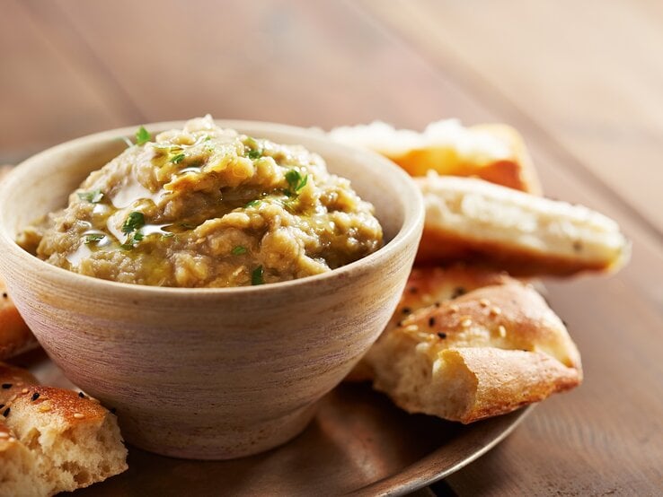 Eine Schale Lib el Kousa, ein levantinischer Zucchini-Knoblauch-Dip, auf einem Tablett, darauf außerdem Fladenbrot-Stücke.