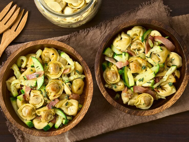 Zwei Holzschüsseln mit Tortellinisalat mit Zucchini und Speck.