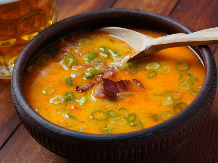 Eine schwarze Schale mit der Cheddar-Bier-Suppe auf einem Holztisch von schräg oben fotografiert.