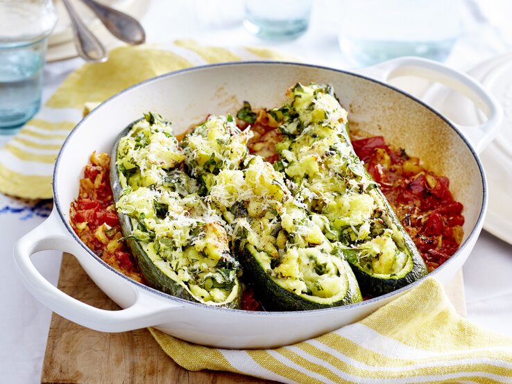 gefüllte Zucchini-Boote mit Kartoffelfüllung auf Tomatengemüse in einer runden Auflaufform.