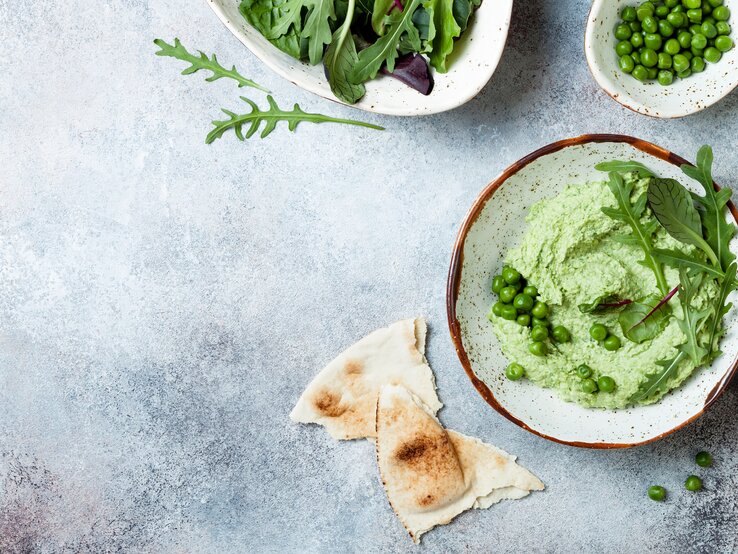 Erbsen-Guacamole garniert mit Rucola in Schüssel vor blauem Untergrund