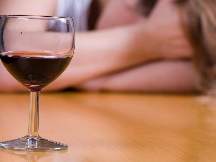 Ein Glas Rotwein auf dem Tisch, im Hintergrund eine verschwommene Person mit langen Haaren.