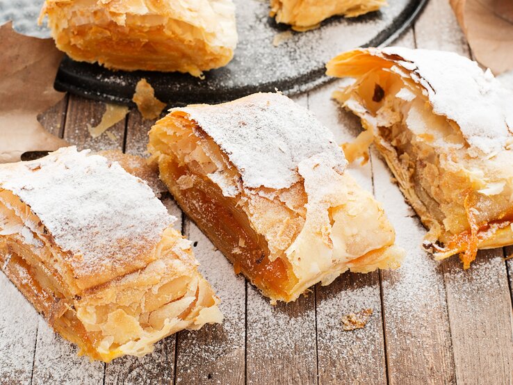 Leckerer Kürbis-Strudel auf einem Holztisch mit Herbstblättern von schräg oben fotografiert.