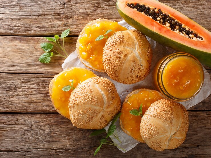 Draufsicht: Drei Brötchen mit einem selbst gemachten Papaya-Aufstrich auf einem Untergrund aus Holz. Daneben liegt eine aufgeschnitten Frucht.