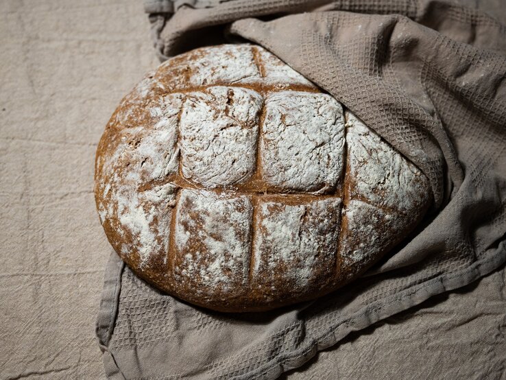 Draufsicht, schräg: Ein Hopfenbrot, das zu Hälfte in einem brauen Leinentuch eingeschlagen ist.