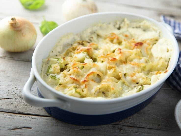 Blumenkohl-Zwiebel-Gratin in weißer Auflaufform auf hölzernem Untergrund. 