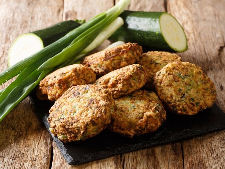 Eine schwarze Schieferplatte mit Zucchini-Feta-Kugeln oben drauf.