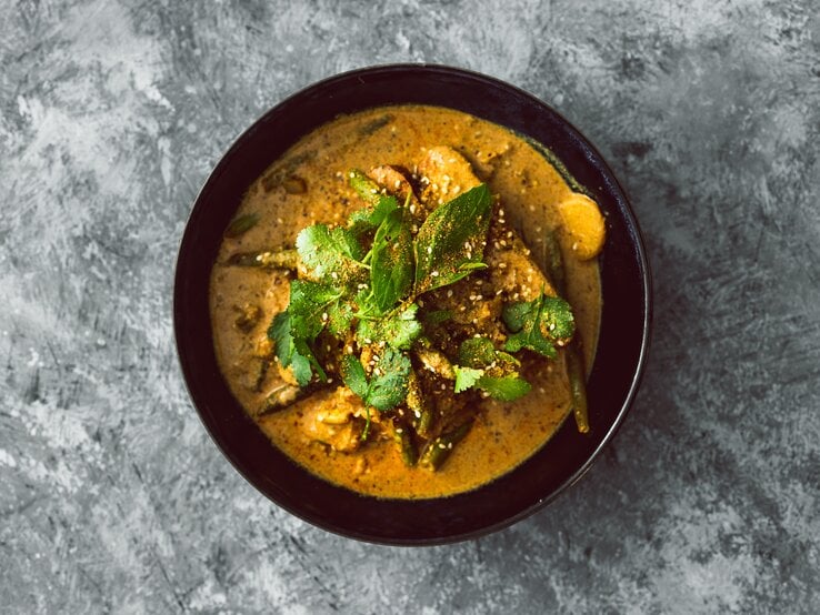 Draufsicht: eine schwarze Schüssel Koriander-Curry mit Tofu steht auf einem grau-weißem Untergrund.